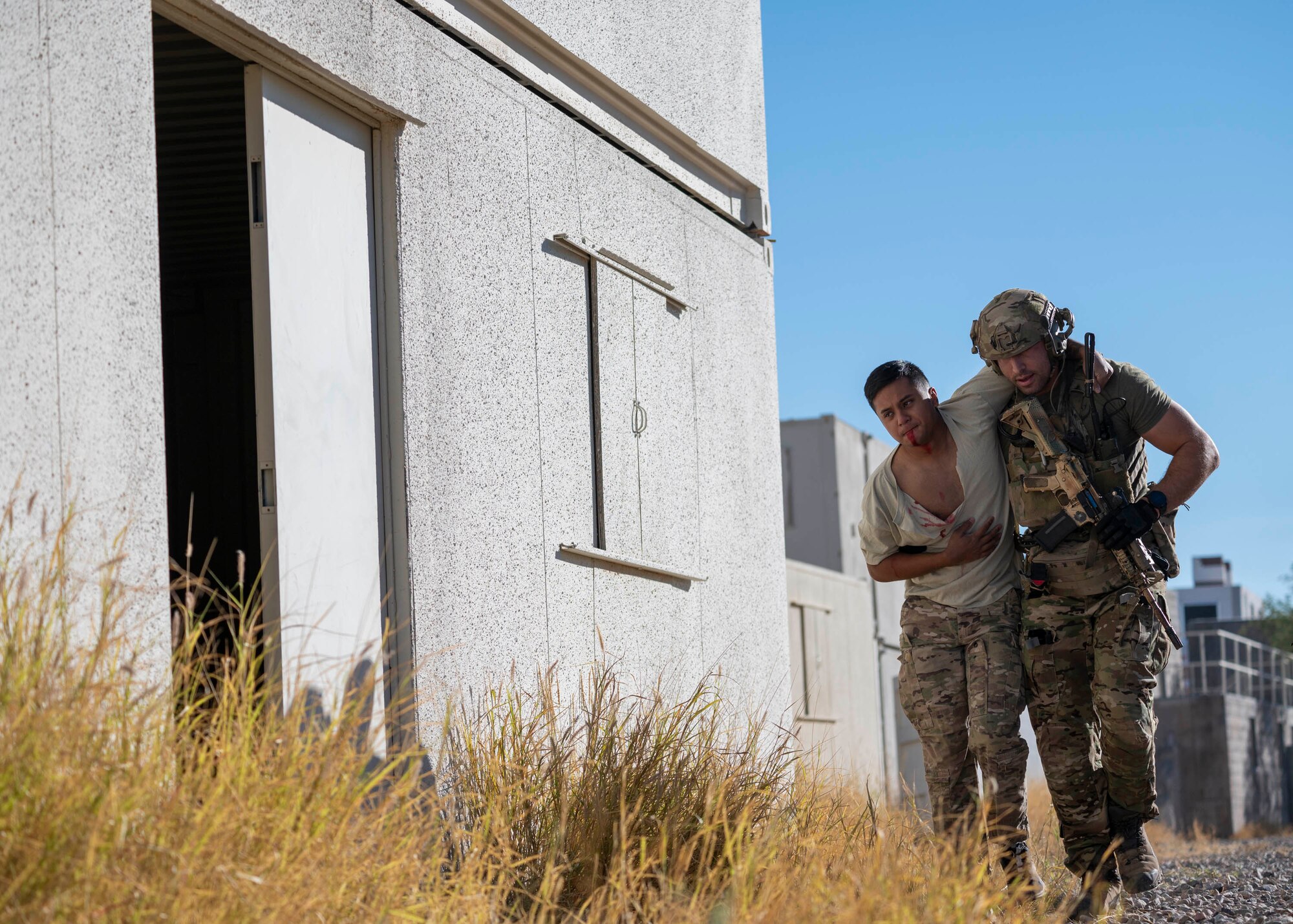 A man in military clothing leads a simulated casualty to a safe place for treatment.