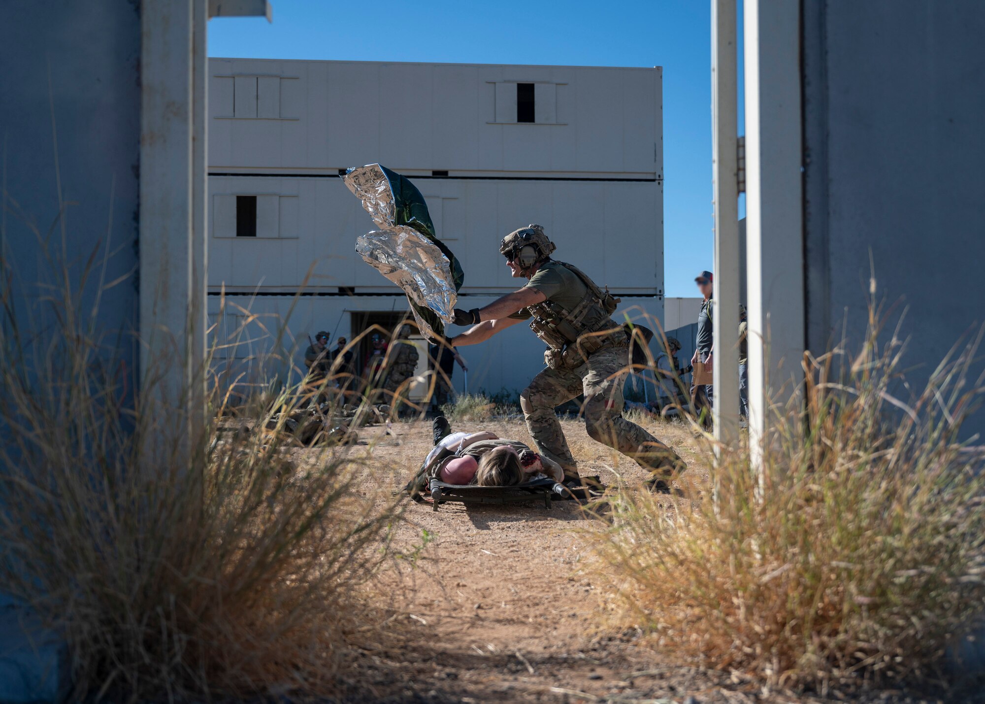 A man in military clothing throws out a blanket in the air above a simulated casualty on the ground.