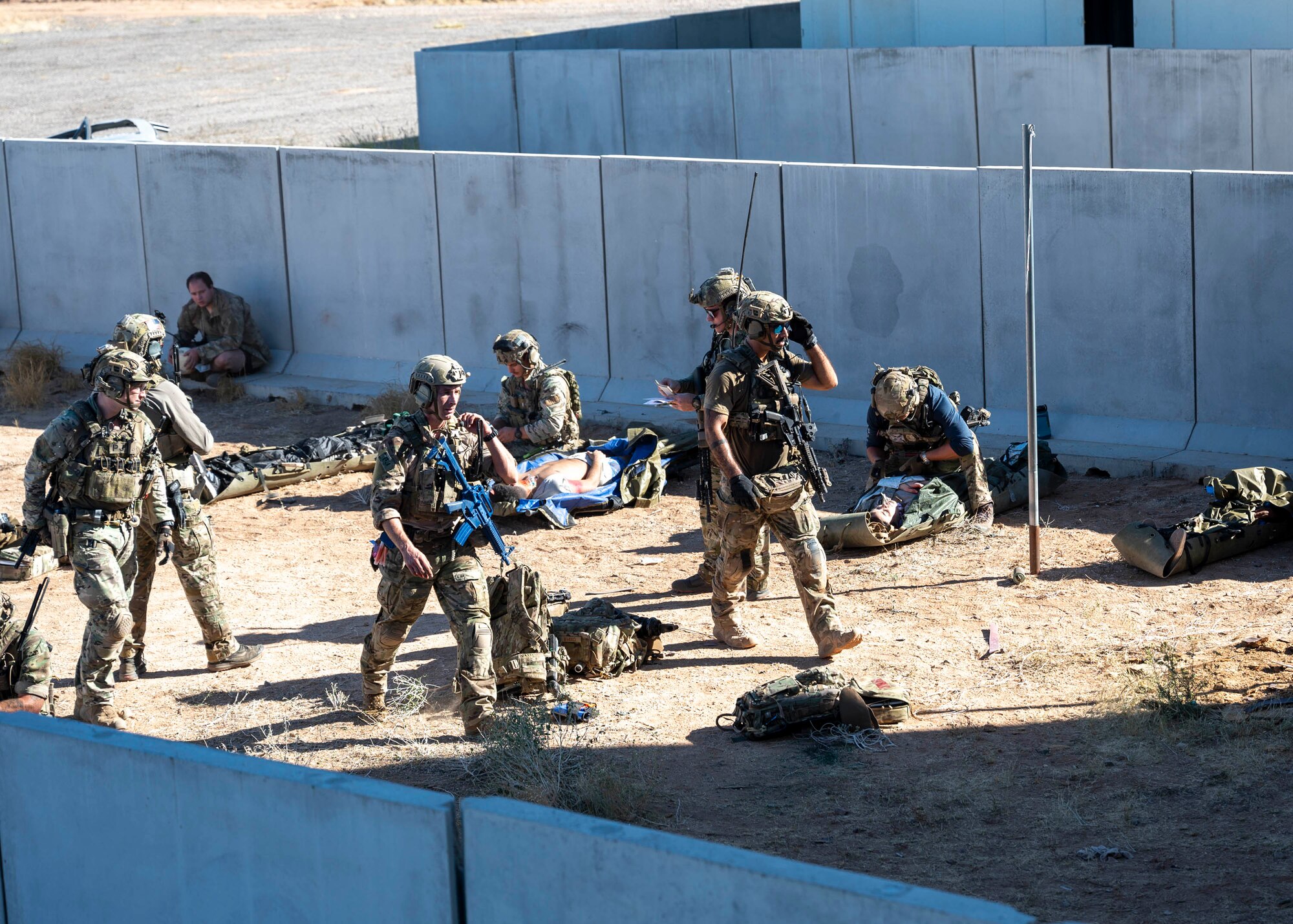 A group of men in military clothing walk between simulated casualties to provide medical care.