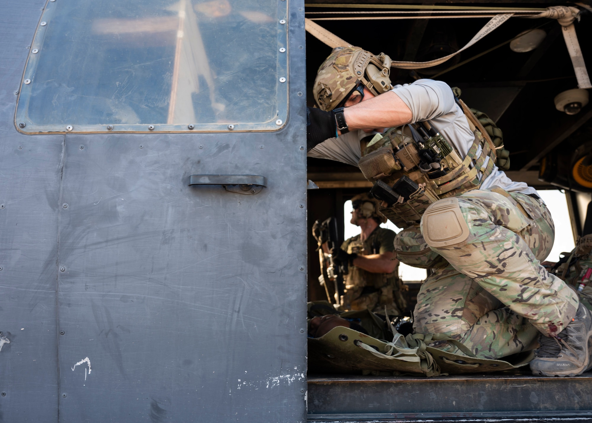 A man in military clothing slides a helicopter door closed.