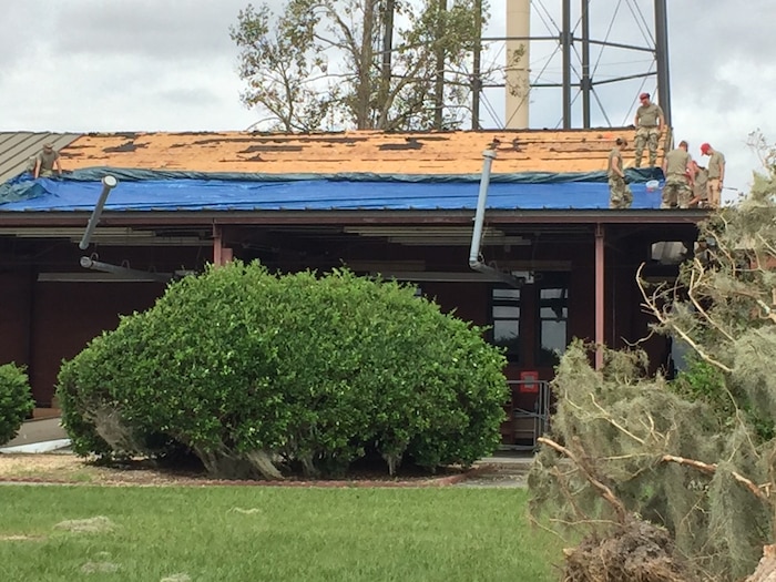 Members of the 823rd RED HORSE Squadron secure tarps on a damaged facility