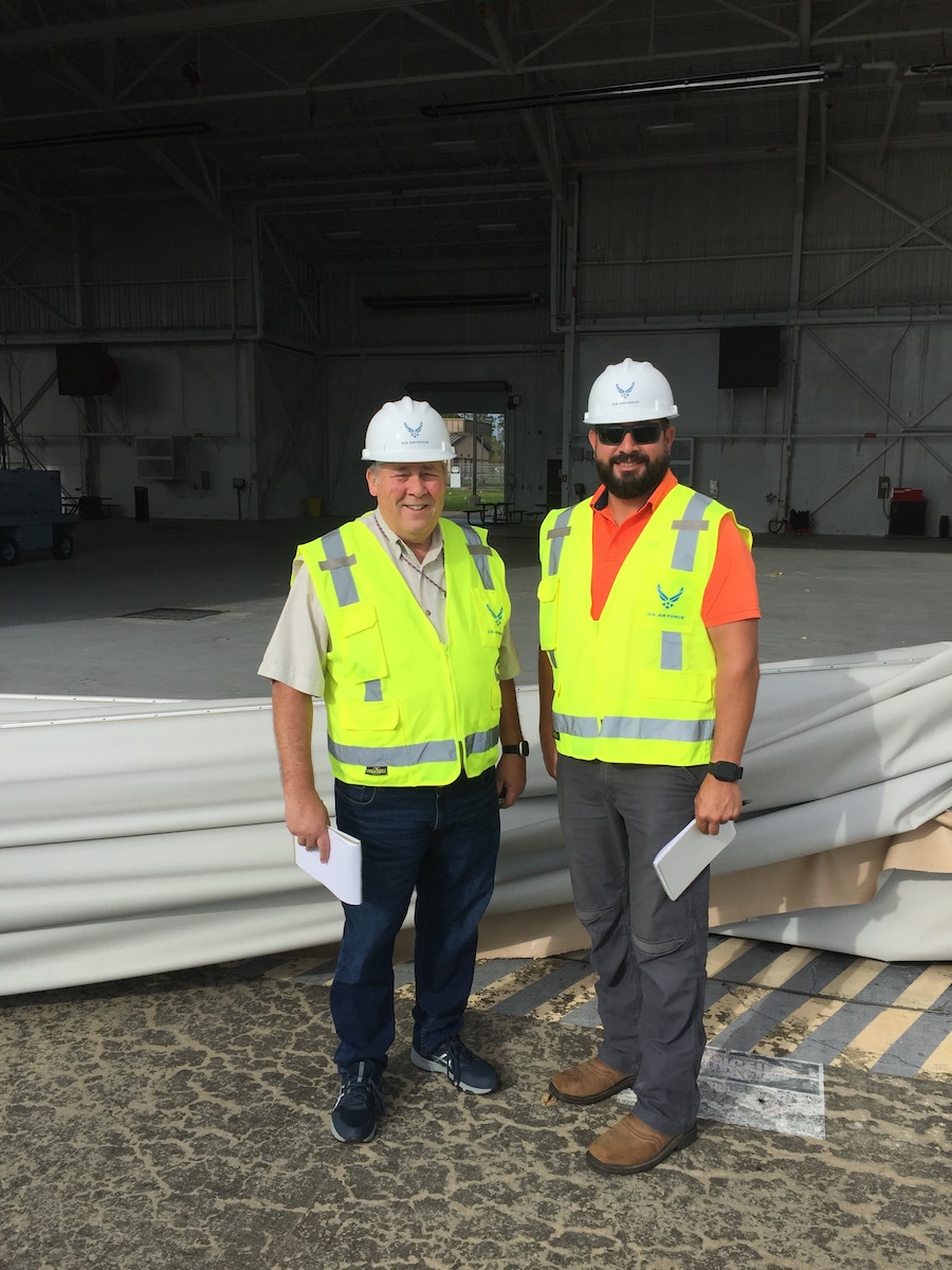 Two Air Force civilians standing in front of a damaged hangar after major storm