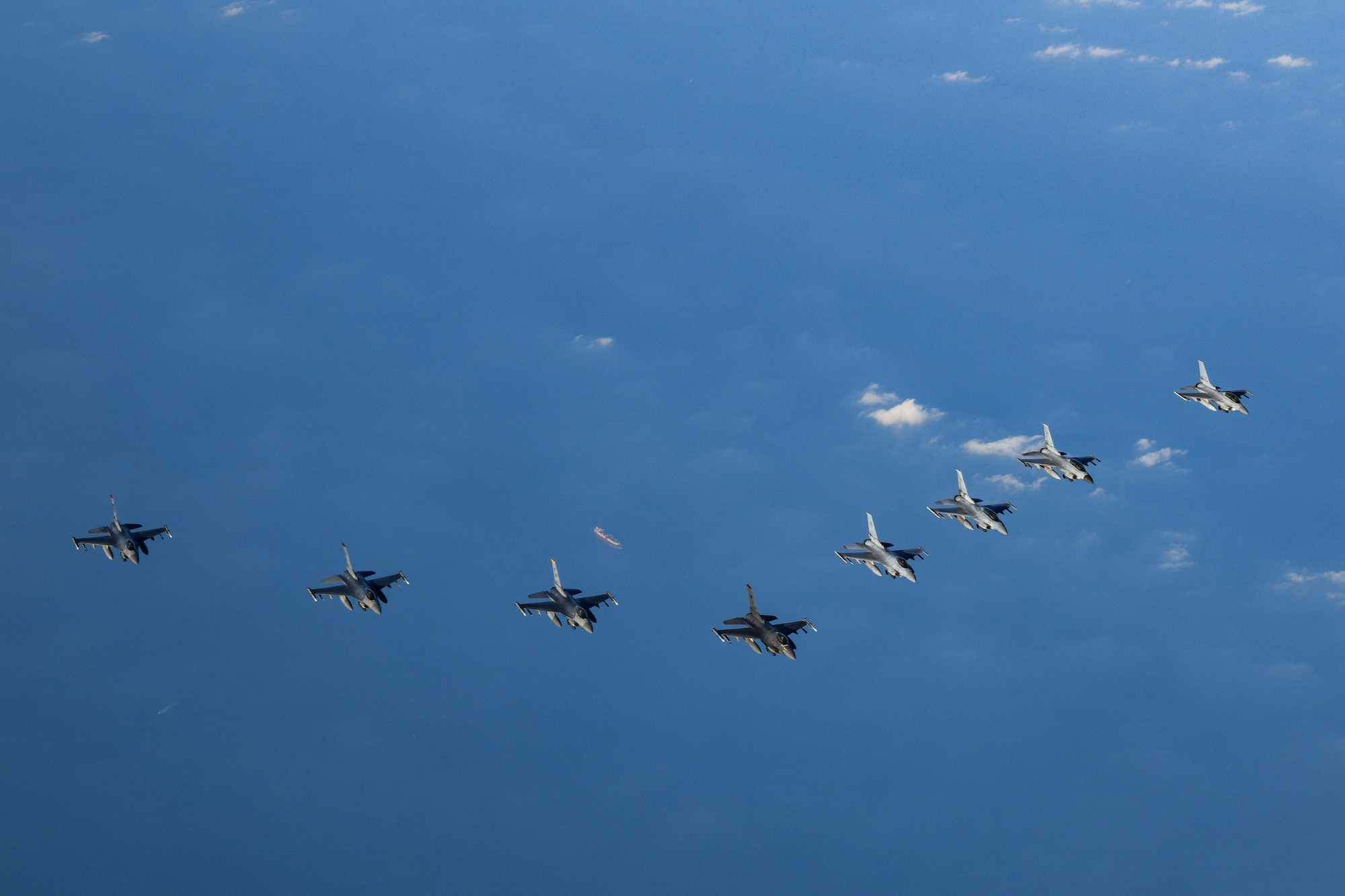 Four U.S. F-16 fighter jets flew alongside four ROK F-16 fighter jets, as seen from above, flying over blue water with clouds.