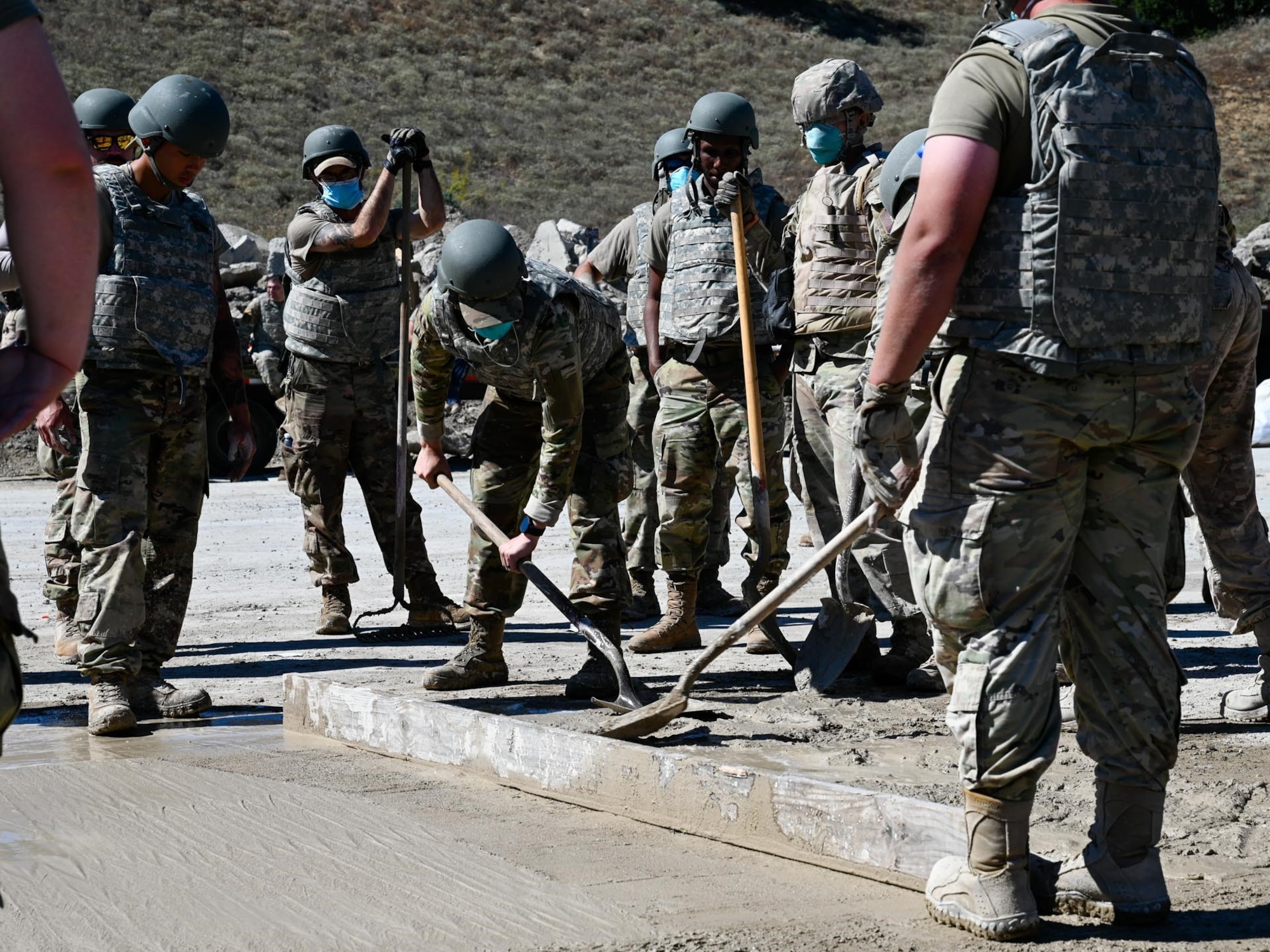 A group of airmen smooth freshly poured concrete.