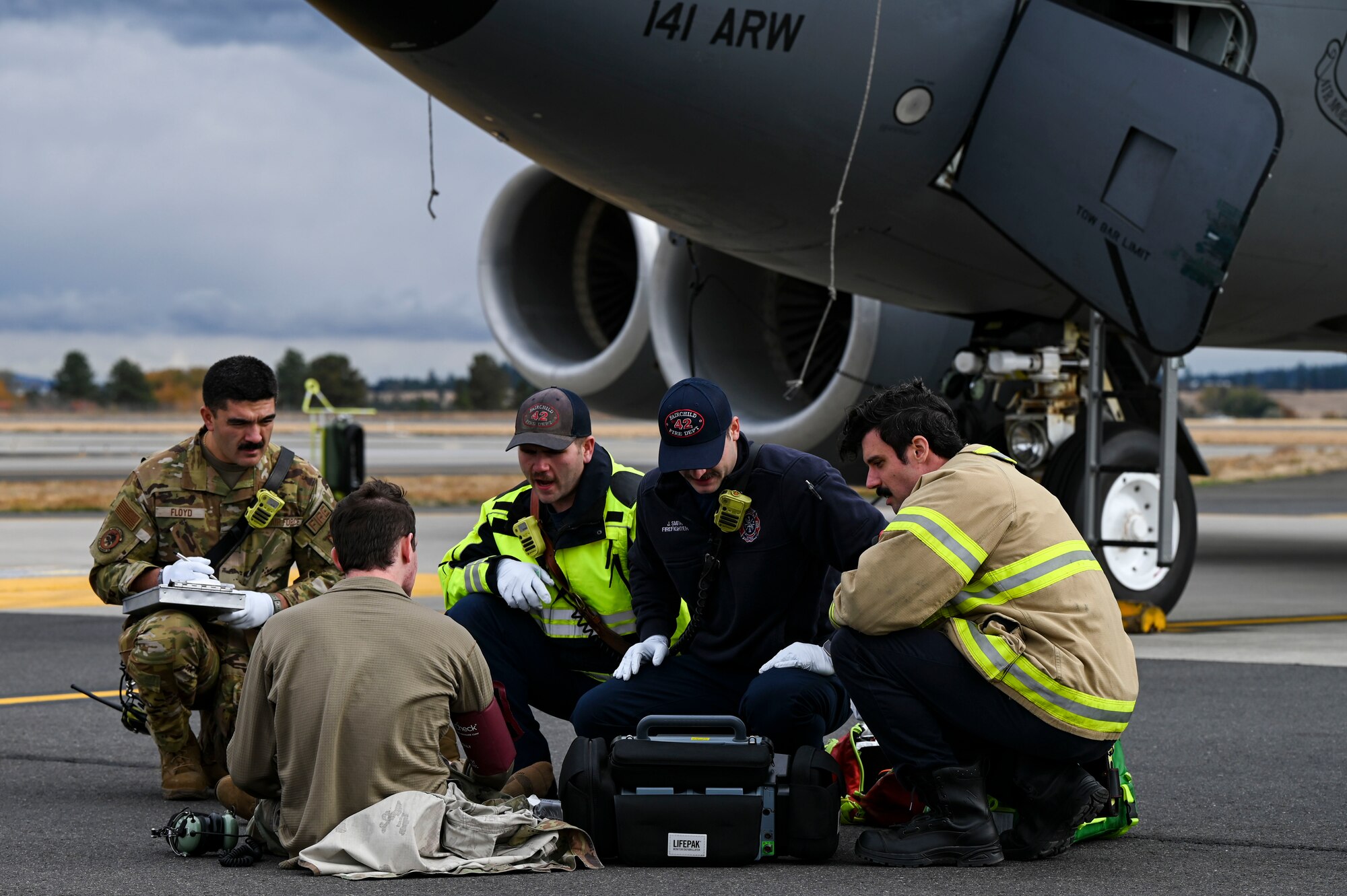 Firefighters huddle around an Airman.