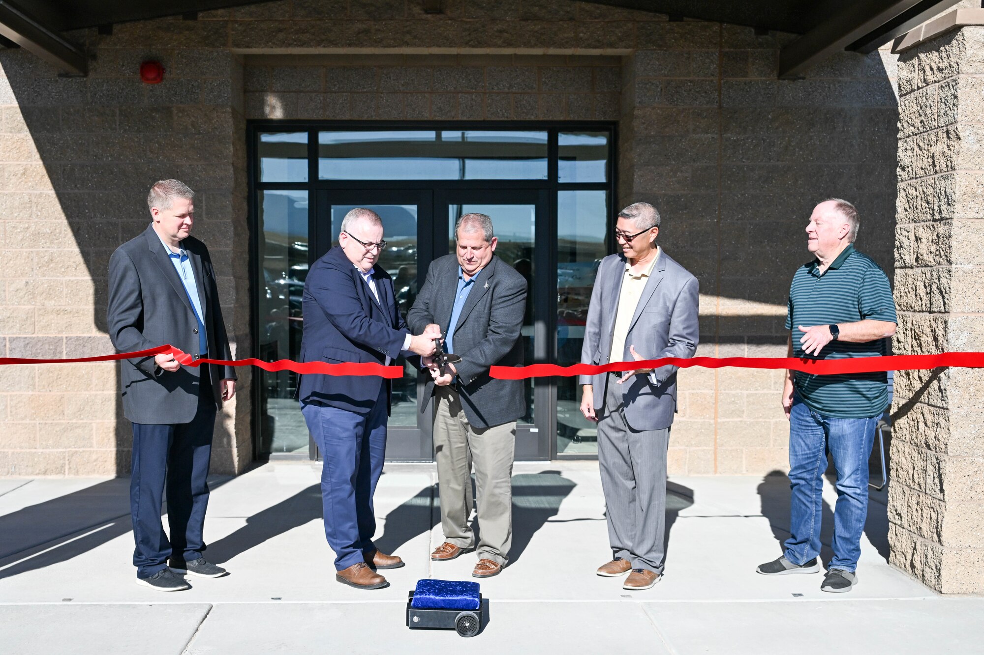 Five people stand in front of a new building and cut the ceremonial ribbon.