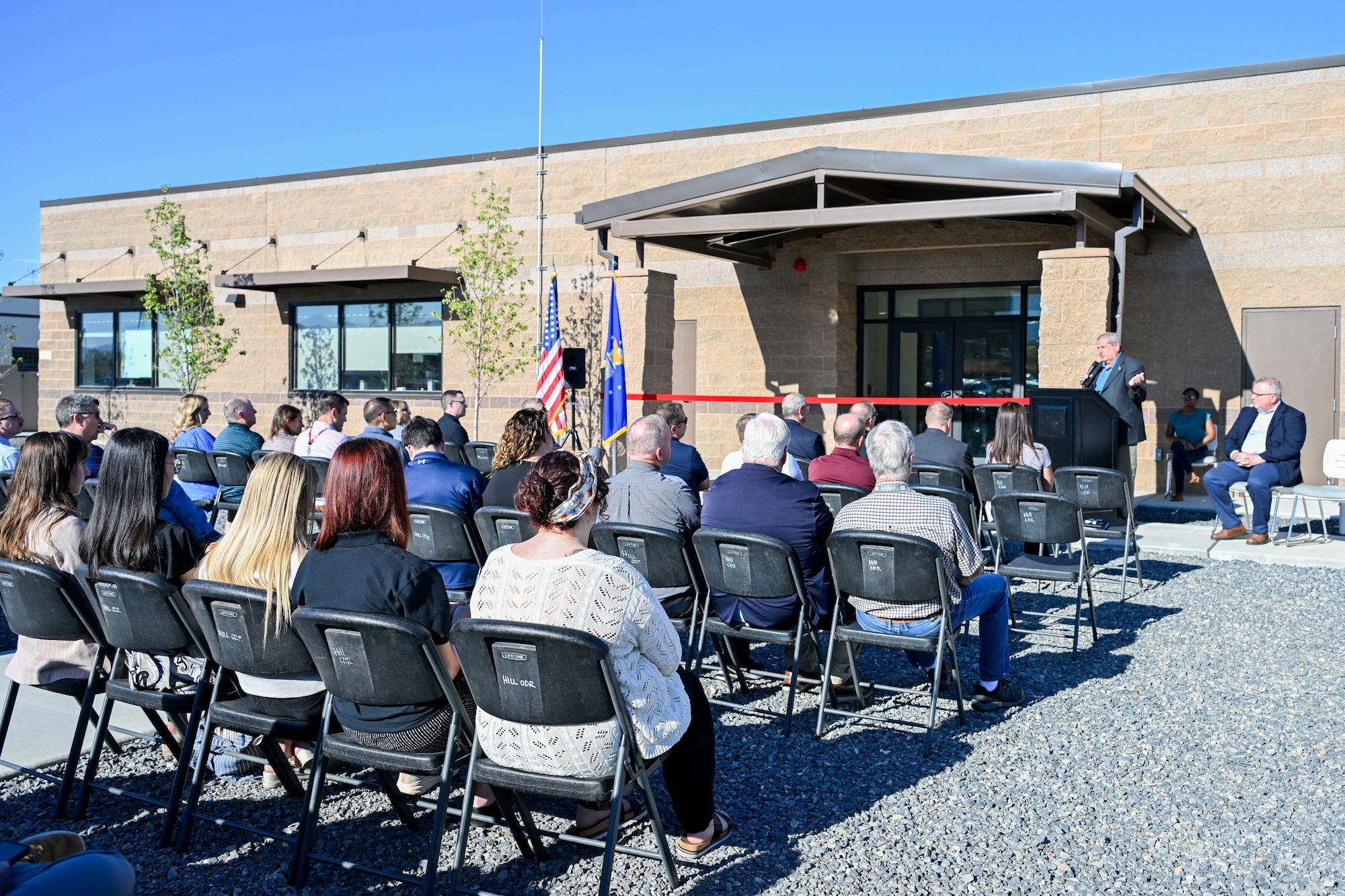 A crowd of people listen to a speaker at a dedication ceremony