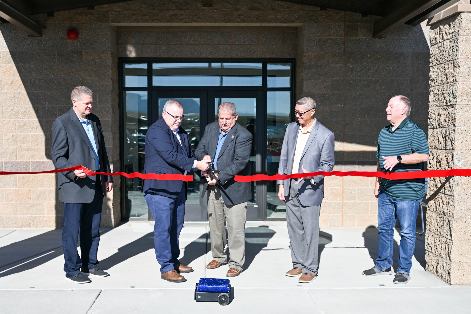 Five people stand in front of a new building and cut the ceremonial ribbon.