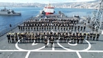 An overhead group shot of dozens of military personnel on a ship.