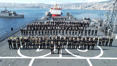 An overhead group shot of dozens of military personnel on a ship.