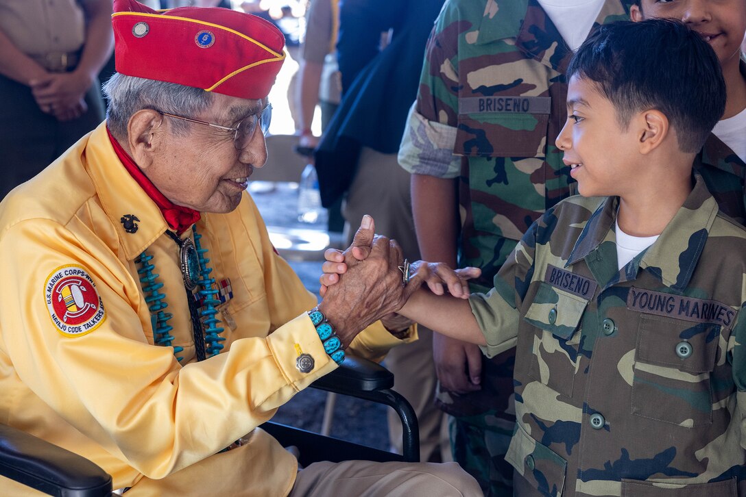 A Marine Corps veteran shakes hands with a child dressed in a Young Marines camouflage uniform.