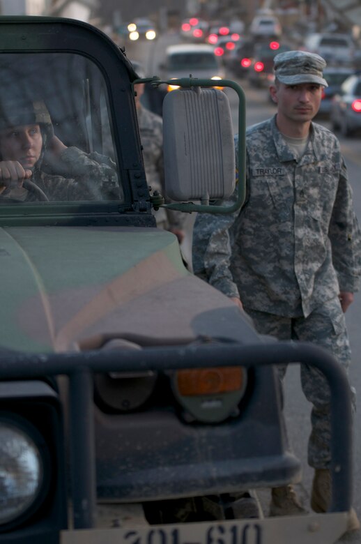 Staff Sgt. Chris Traylor walks up the line of a Kentucky National Guard convoy, March 6, in West Liberty, Ky., while Pfc. Mary Lewis waits for her turn to fuel up her Humvee at a fueling checkpoint. Both soldiers spent the day patrolling the area to ensure residents and business owners who were let in for clean-up operations remained safe.