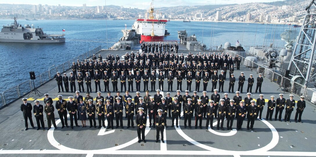 An overhead group shot of dozens of military personnel on a ship.
