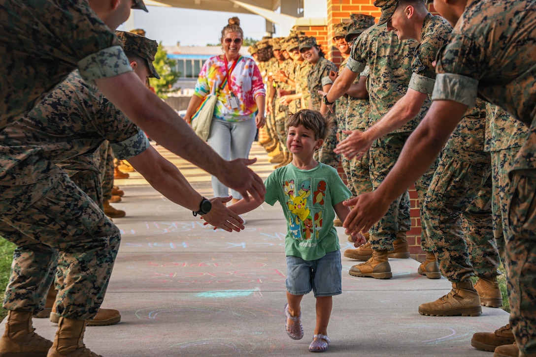 A child high-fives rows of Marines on either side of a walkway while a parent follows behind.