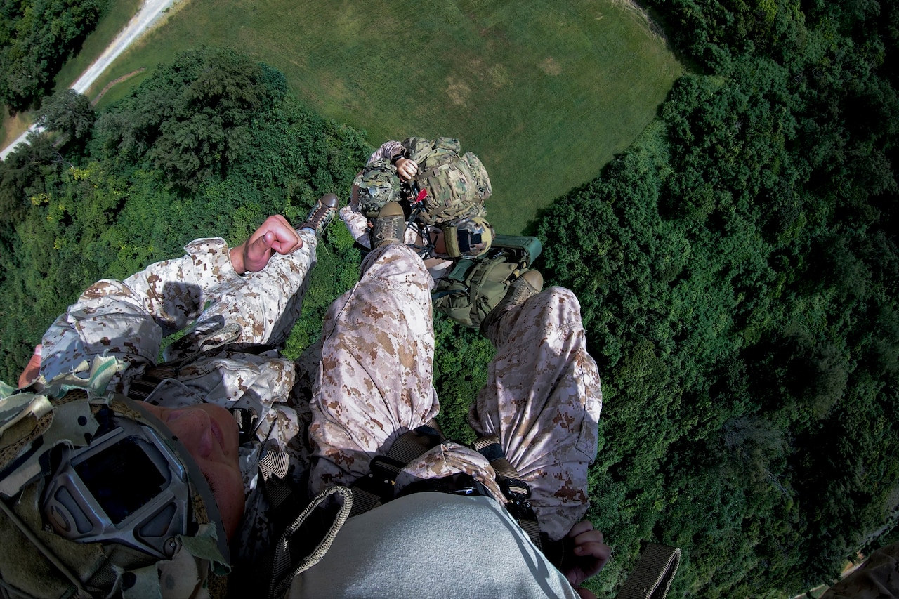 Marines suspend in the air from a UH-1Y Venom helicopter over trees.