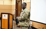 Smiling man, who is standing up and talking, wears a military uniform