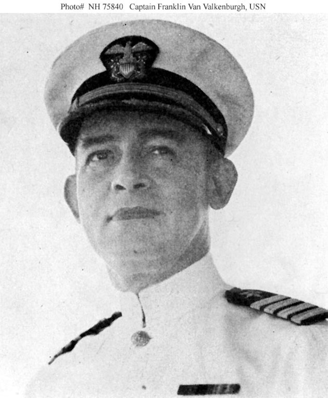 A Navy officer in white uniform and cap poses in a photo.