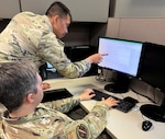 Two Airmen look at computer screen.