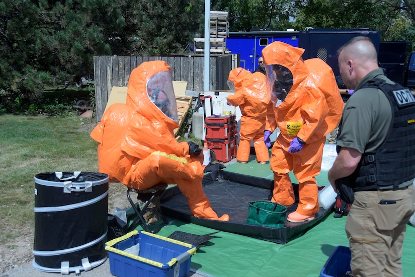 National Guardsmen sit and stand in biohazard suits.