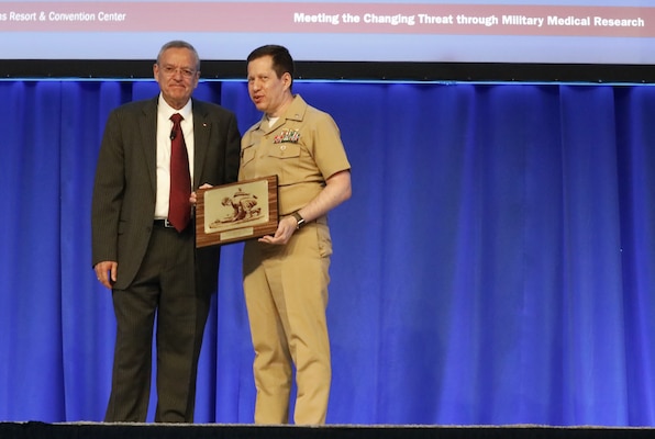 KISSIMMEE, Fla. (Aug. 26, 2024) Capt. Jonathan Stahl, former commanding officer of Naval Medical Research Unit (NAMRU) INDO PACIFIC, accepts the 2024 Outstanding Research Accomplishment Team Award at the opening ceremony of the Military Health System Research Symposium (MHSRS) on behalf of the Long-Term Immunity Against Novel and Known Strains of SARS-CoV-2 Study team. Stahl handed off leadership of the command earlier this summer, ahead of his retirement later this month, after 30 years with the U.S. Navy. MHSRS is the Department of Defense's premier scientific meeting that focuses specifically on the unique medical needs of service members. This annual educational symposium brings together healthcare professionals, researchers, and DoD leaders for four days of critical learning, intensive idea sharing and relationship building. Navy Medicine Research and Development attended MHSRS and participated in breakout sessions, poster presentations, lectures, and manned booths in the exhibit hall. The eight Navy Medicine Research and Development commands, led by Naval Medical Research Command (NMRC), and consisting of Naval Health Research Center (NHRC), Naval Submarine Medical Research Laboratory (NSMRL) and NAMRUs Dayton, San Antonio, EURAFCENT, INDO PACIFIC, and SOUTH, are engaged in a broad spectrum of activity from basic science in the laboratory to field studies in austere and remote areas of the world to investigations in operational environments. In support of the Navy, Marine Corps and joint U.S. warfighters, researchers study infectious diseases, biological warfare detection and defense, combat casualty care, environmental health concerns, aerospace and undersea medicine, medical modeling, simulation, operational mission support, epidemiology and behavioral sciences. (U.S. Navy Photo by Sidney Hinds/released)