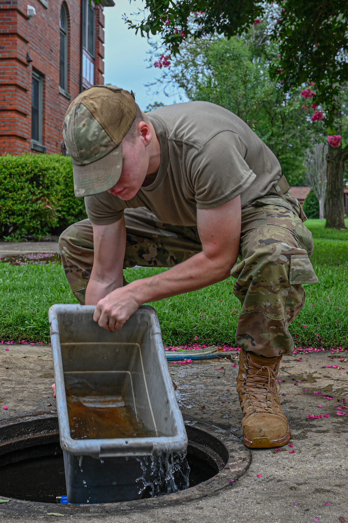 Photo of an Airman collecting water from a manhole with a storage bin.