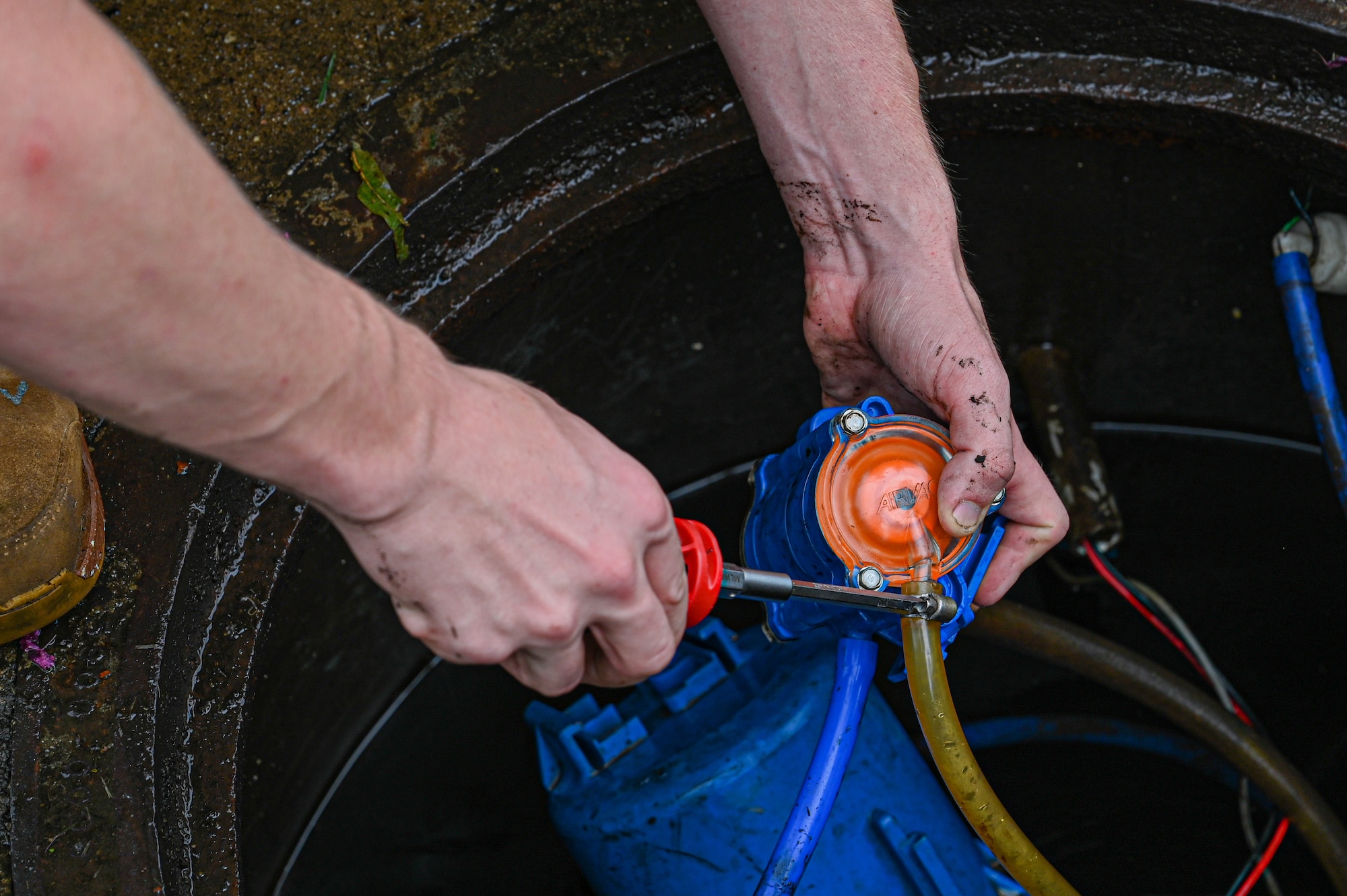 close up of an Airman's hands tightening a screw on a vacuum in a manhole.