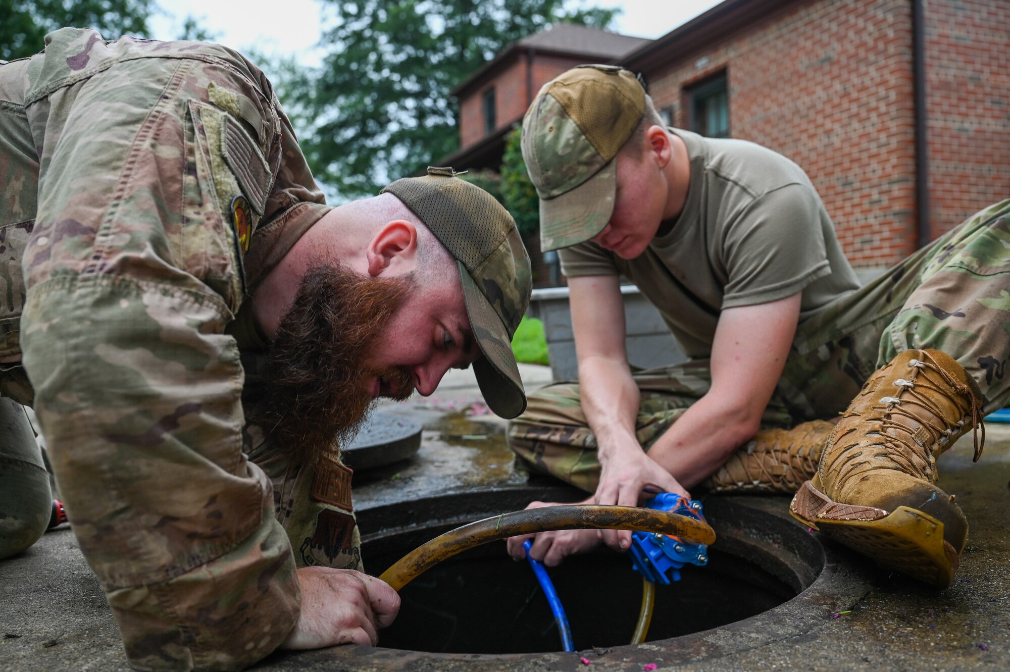 Two Airmen working together on a manhole with pipes coming out.