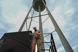 Low angle photo of an Airman collecting water at the bottom of a water tower.
