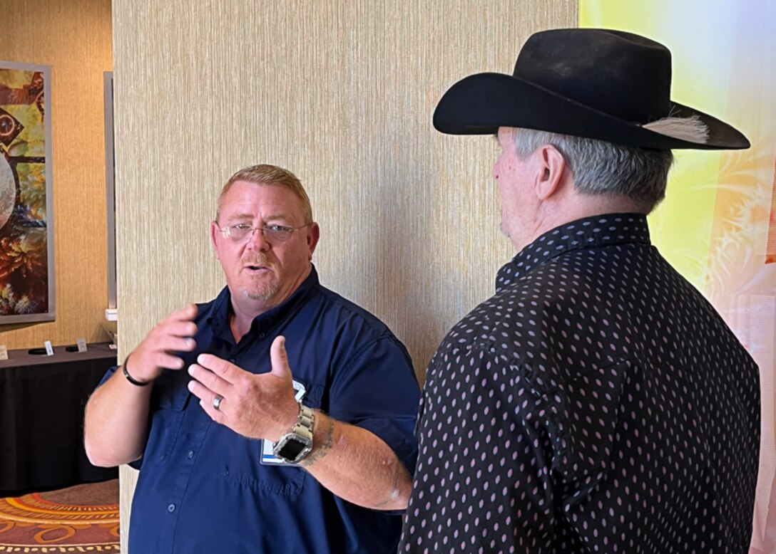 Two men talk in a hallway one is wearing a cowboy hat.