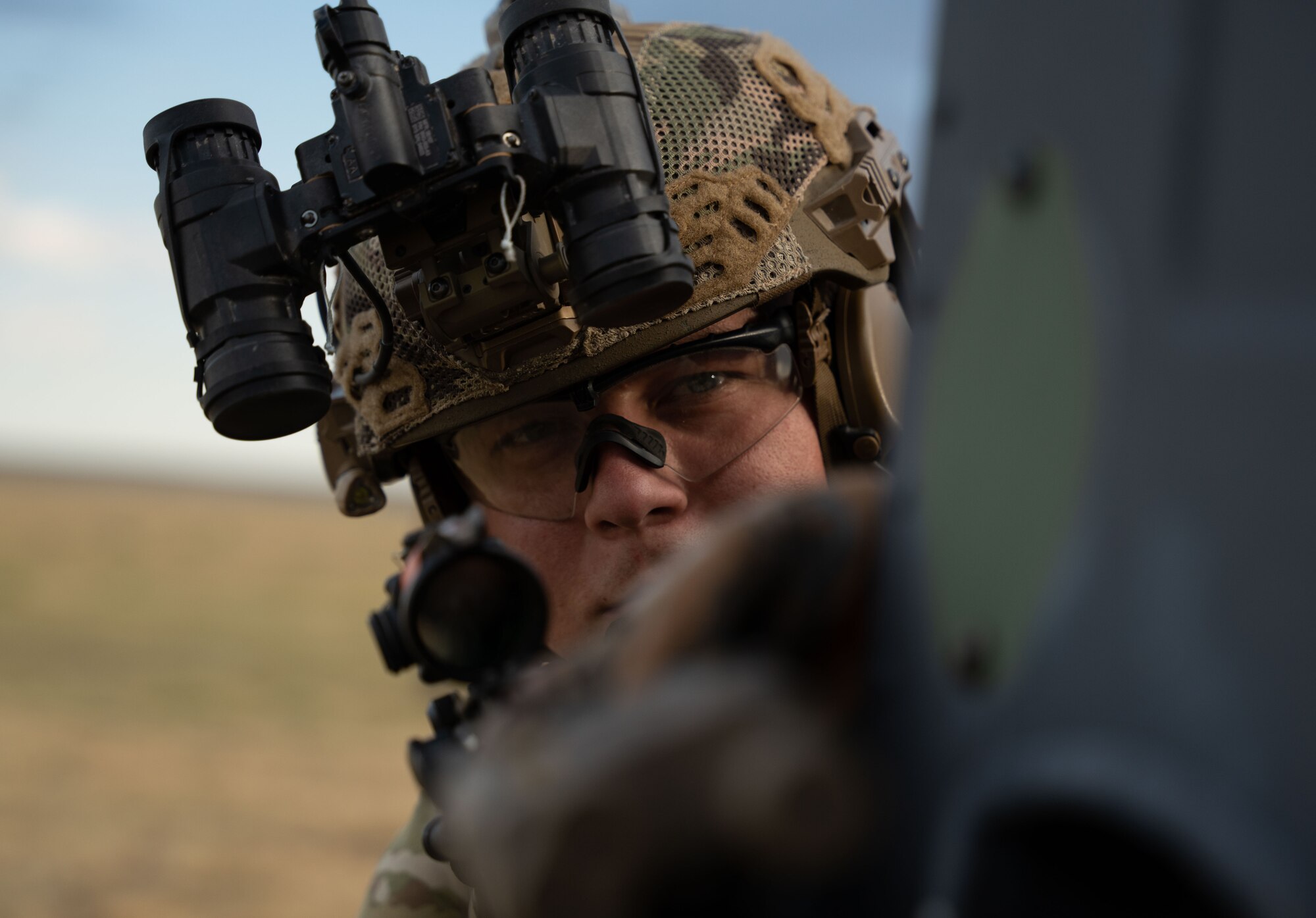 A man in military uniform and military helmet looks down the sights of a rifle.