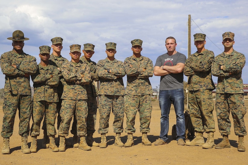 Nine people in military uniforms stand alongside a person in civilian clothing. All are posing with their arms crossed over their chests.