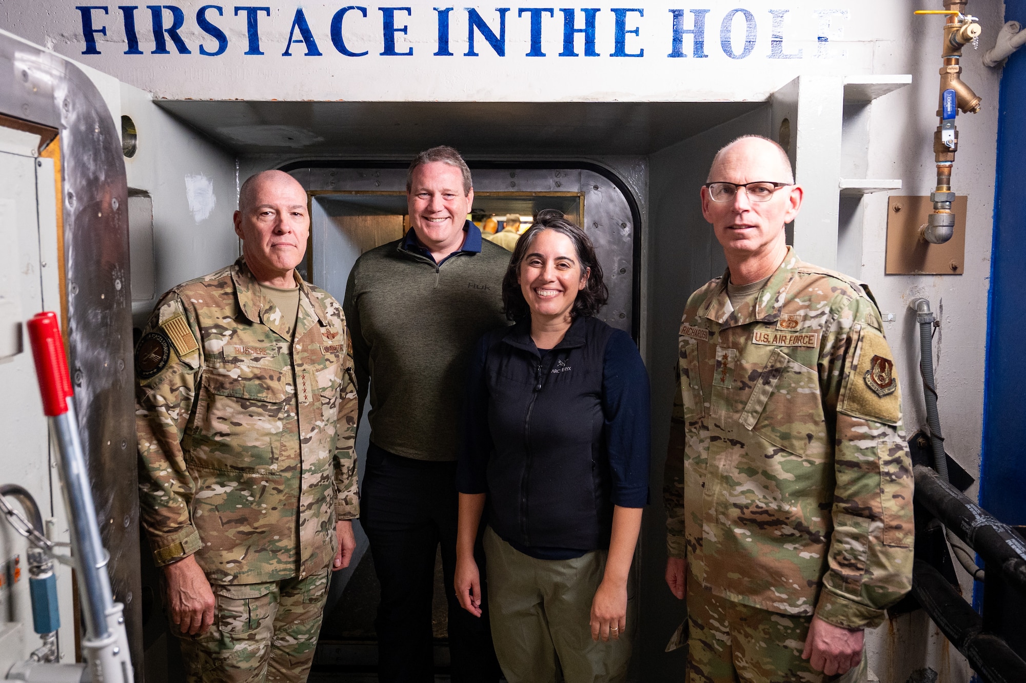 Four people pose for a photo in front of a launch door in a launch control center.