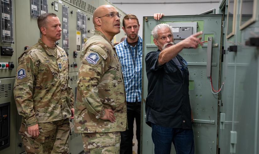 A technician points at equipment while two guardians and another technician looks on.