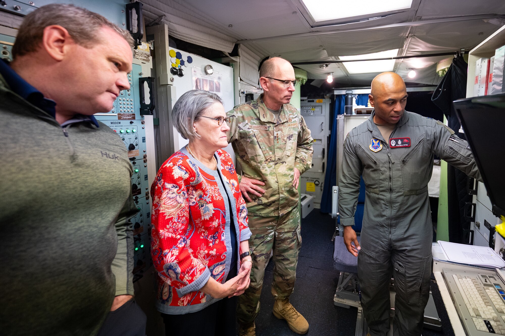 A missileer shows a group of three people something on a screen.