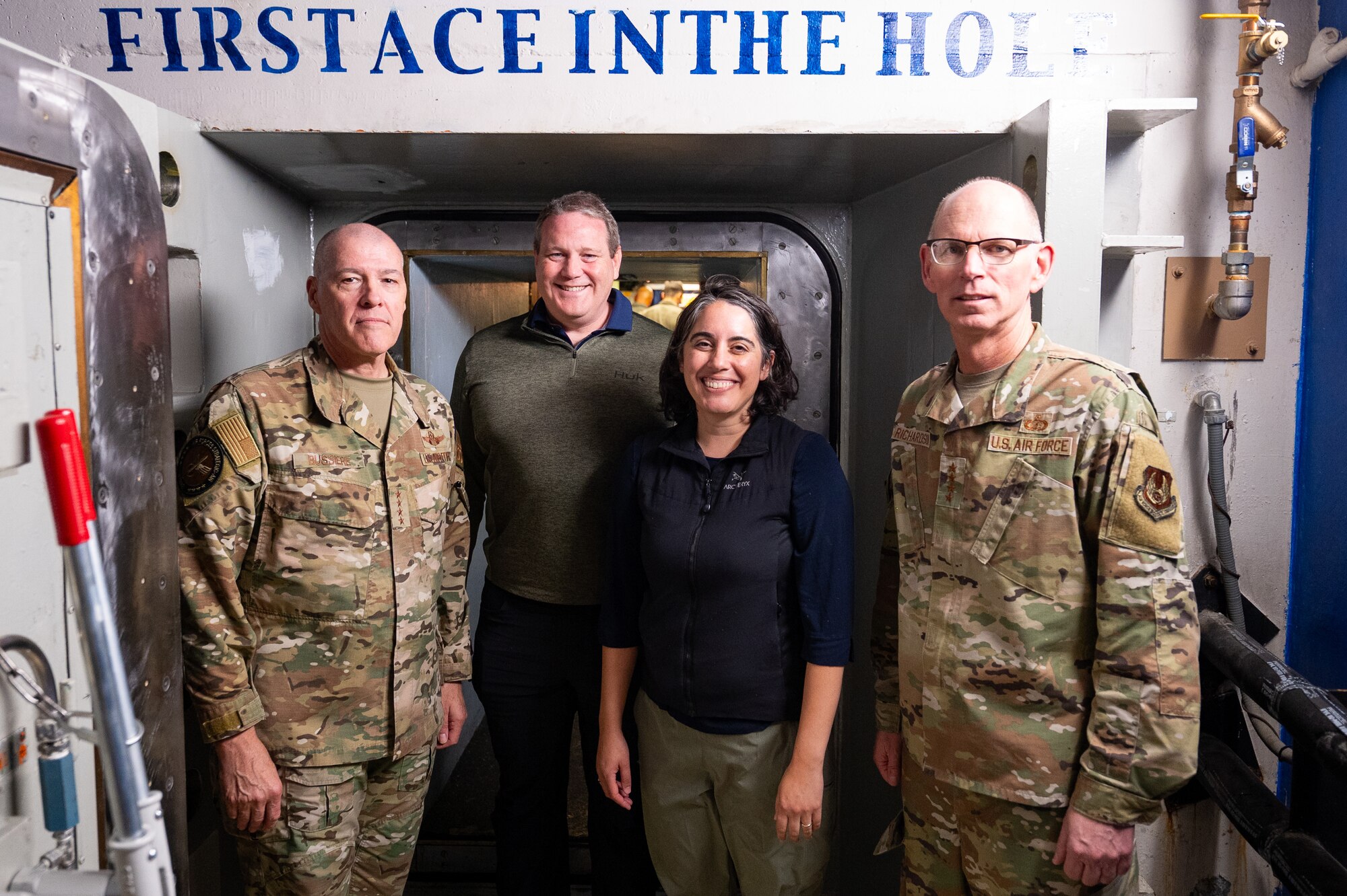 Four people pose for a photo in front of a launch door in a launch control center.