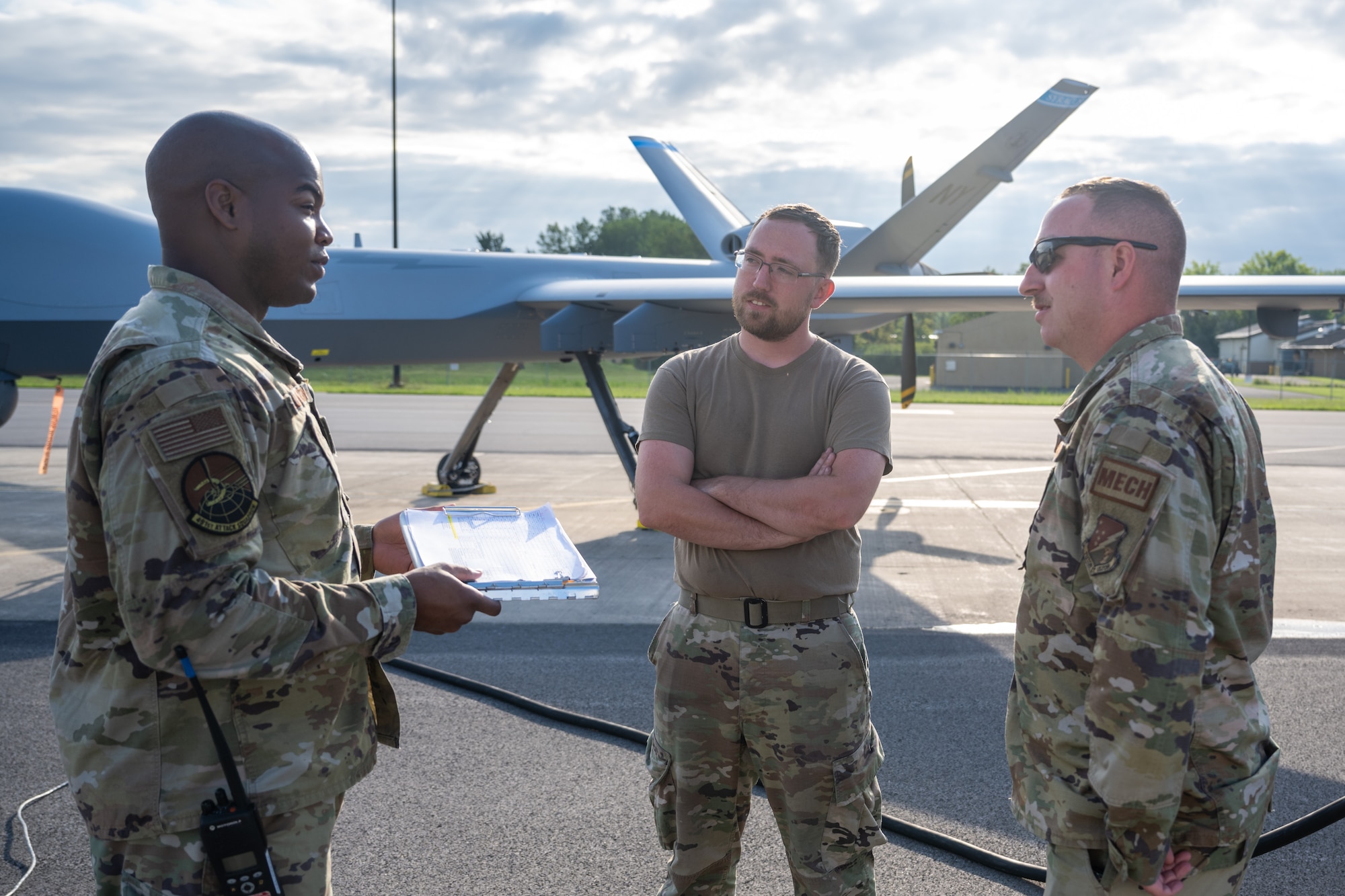 Airmen from Hancock Field Air National Guard Base, New York discuss morning flights near an MQ-9 Reaper at the flightline.