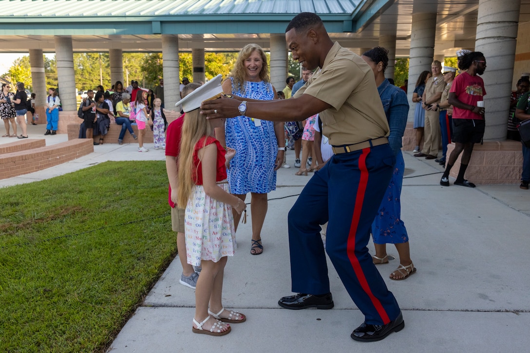 U.S. Marine Corps Lt. Col. Anthony M. Ansley II, right, commanding officer of Combat Logistics Battalion 22, Combat Logistics Regiment 2, 2nd Marine Logistics Group, places his cover on a student's head during a CLB-22 adopt-a-school event at Carolina Forest International Elementary School, in Jacksonville, North Carolina, August 26, 2024. This event welcomed students back to the classrooms, providing extra motivation and well wishes as they start their first day of school following summer break. (U.S. Marine Corps photo by Lance Cpl. Jessica J. Mazzamuto)