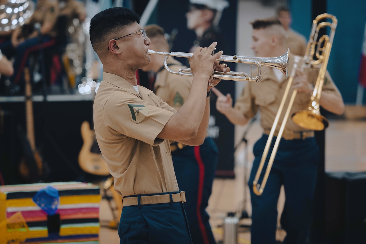 A Marine plays the trumpet inside a gymnasium while other Marines play in the background.