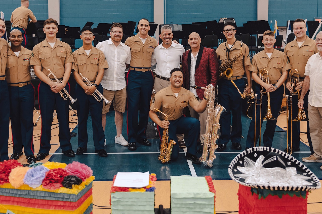 A group of Marines poses with members of a band inside a gymnasium.