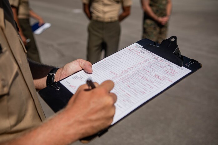 U.S. Marine Corps Staff Sgt. Logan Stogdill, a drill master with 2nd Recruit Training Battalion, Recruit Training Regiment, writes down his evaluations of a platoon with Lima Company, 3rd Recruit Training Battalion during their final drill evaluation at Marine Corps Recruit Depot San Diego, California, Aug. 24, 2024. During the final drill evaluation, the platoons are scored based on their uniforms, bearing, and movements, as well as the senior drill instructor’s cadence, sword control, and movement commands. (U.S. Marine Corps photo illustration by Sgt. Jesse K. Carter-Powell)
