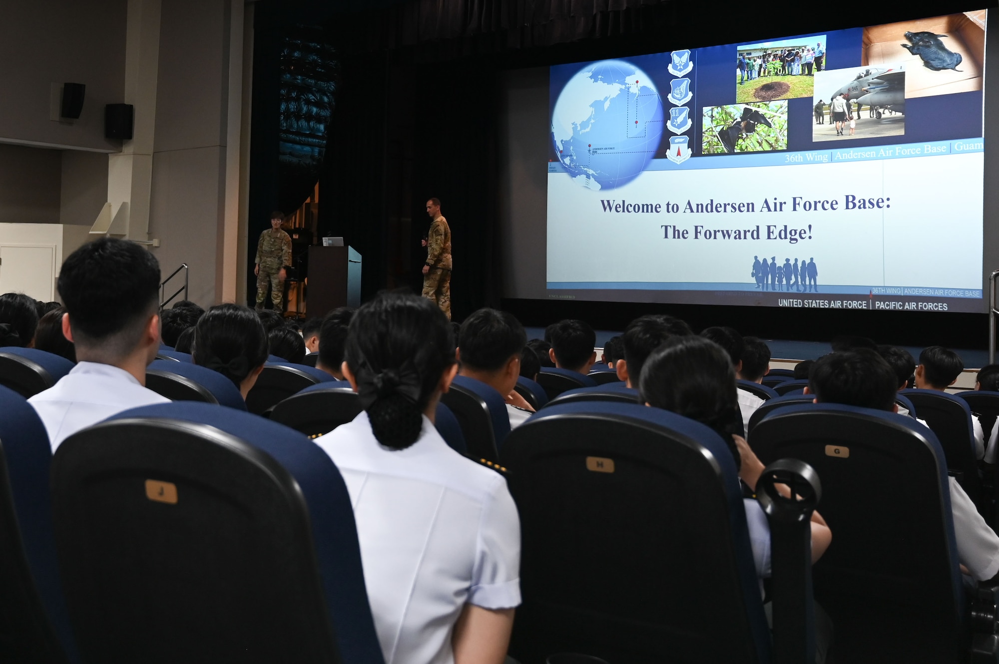 Members of the Republic of Korea Air Force sit and listen to the U.S. Air Force Airman speaking on a stage.