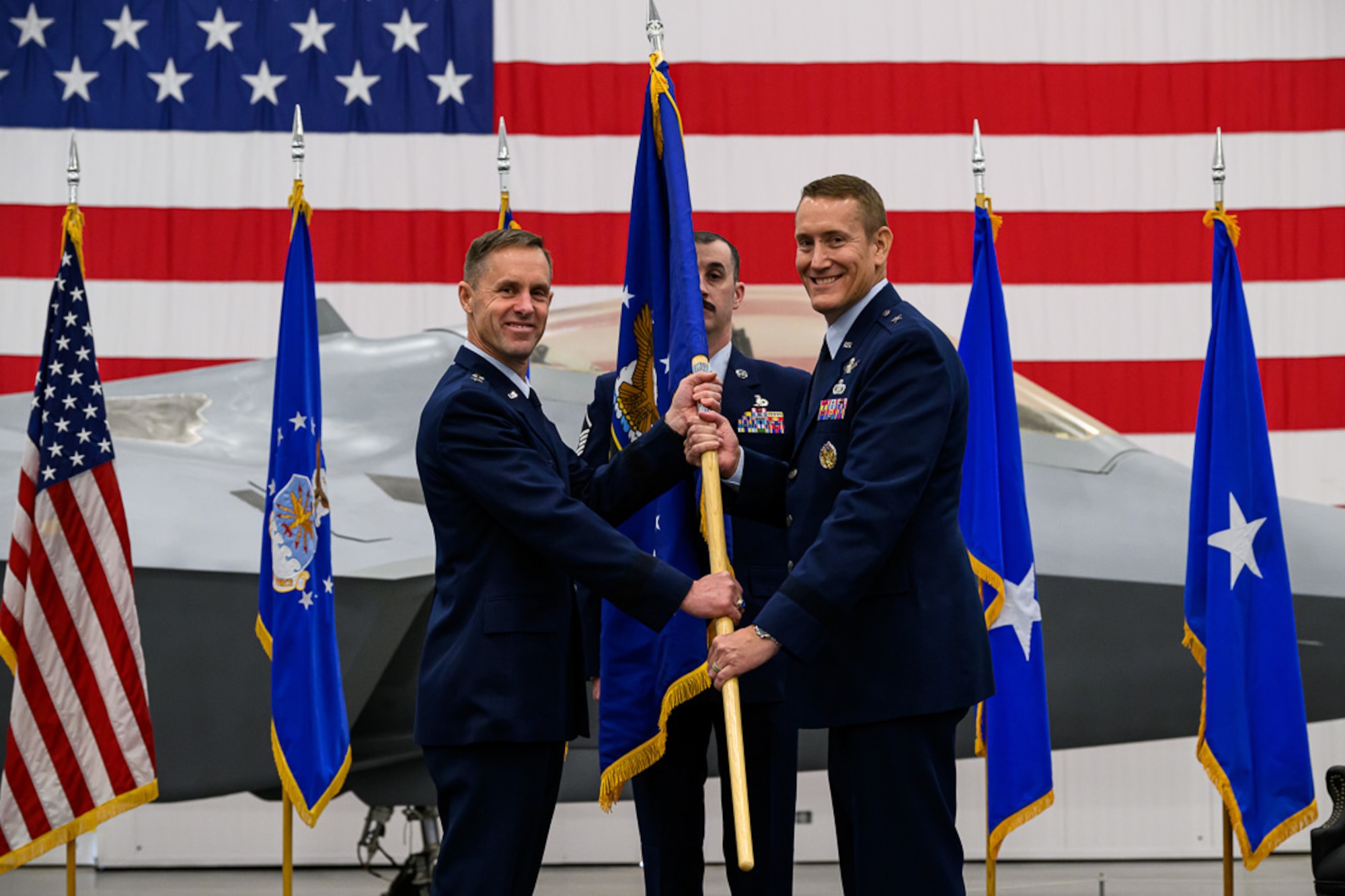 Man in uniform passes a flag to a second man in uniform