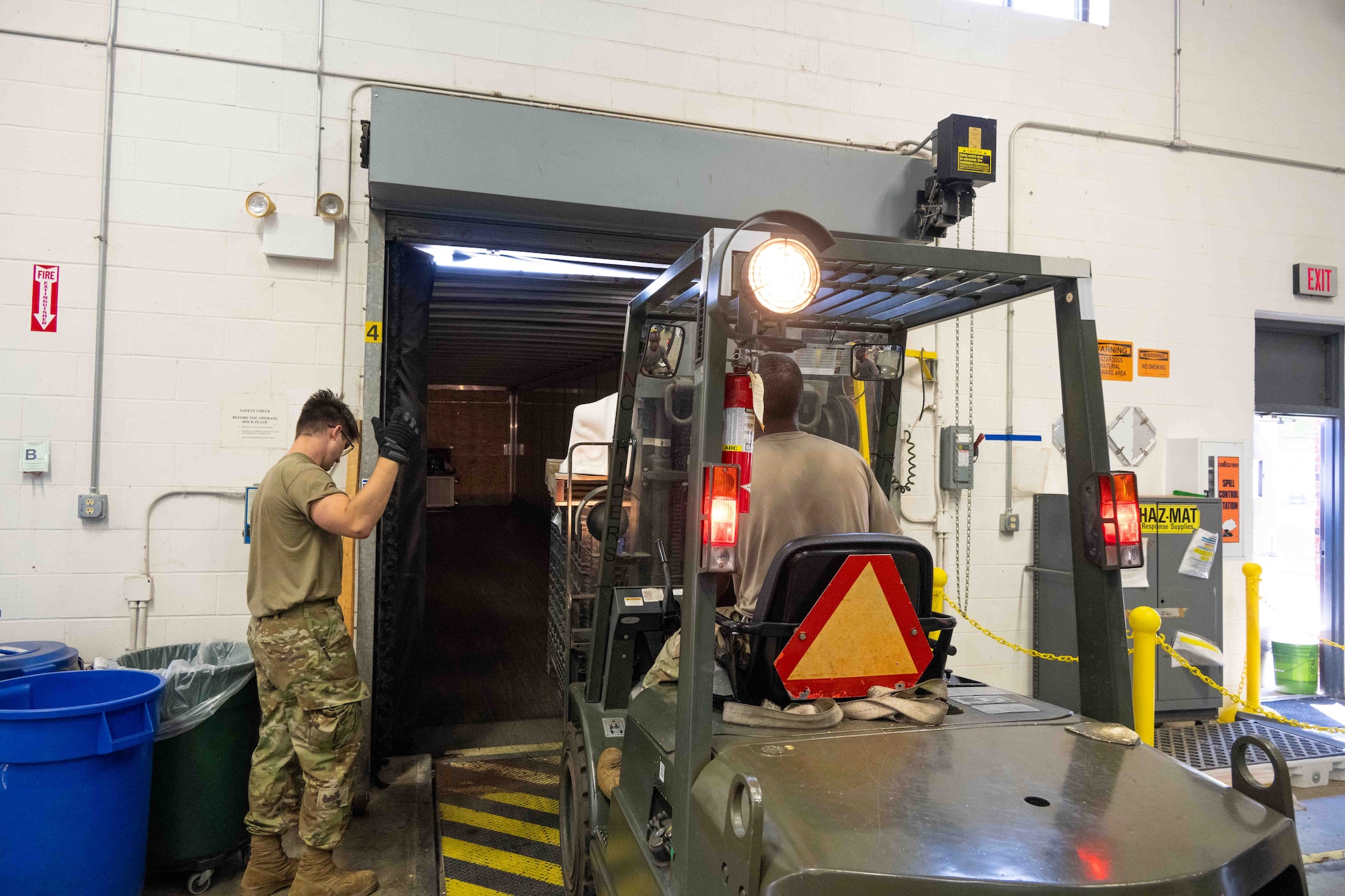 One person guides a forklift driver into the back of a semi truck.