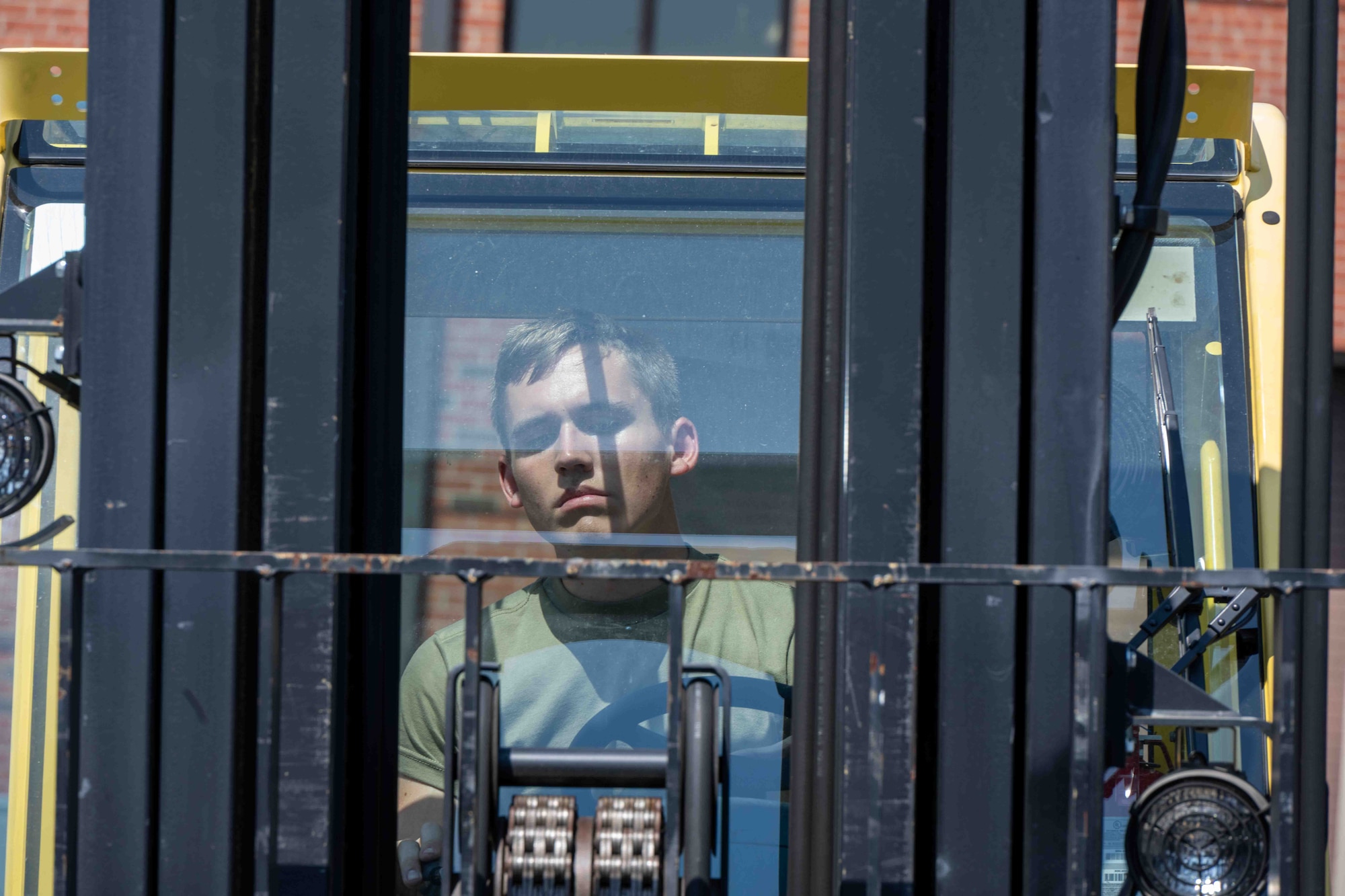A forklift driver's face is seen through the forks and rails of a medium forklift.