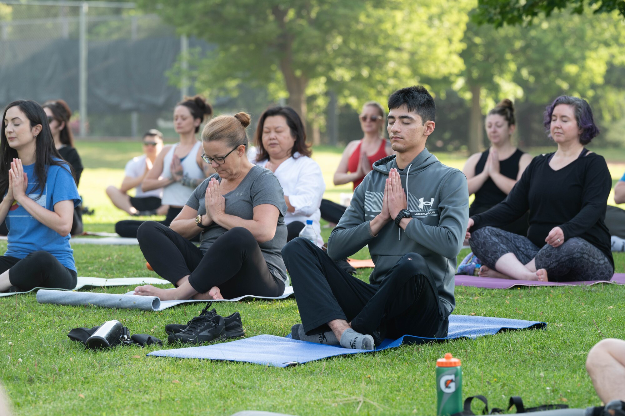 Participants are sitting on mats in the park practicing a yoga move.