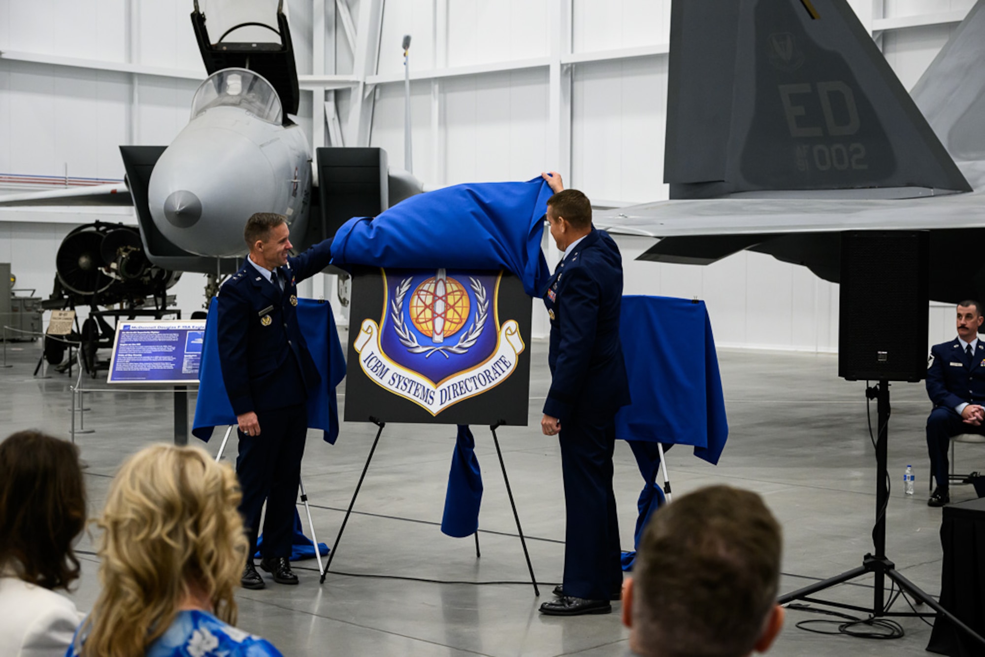 Two men in uniform unveil an emblem on a display stand