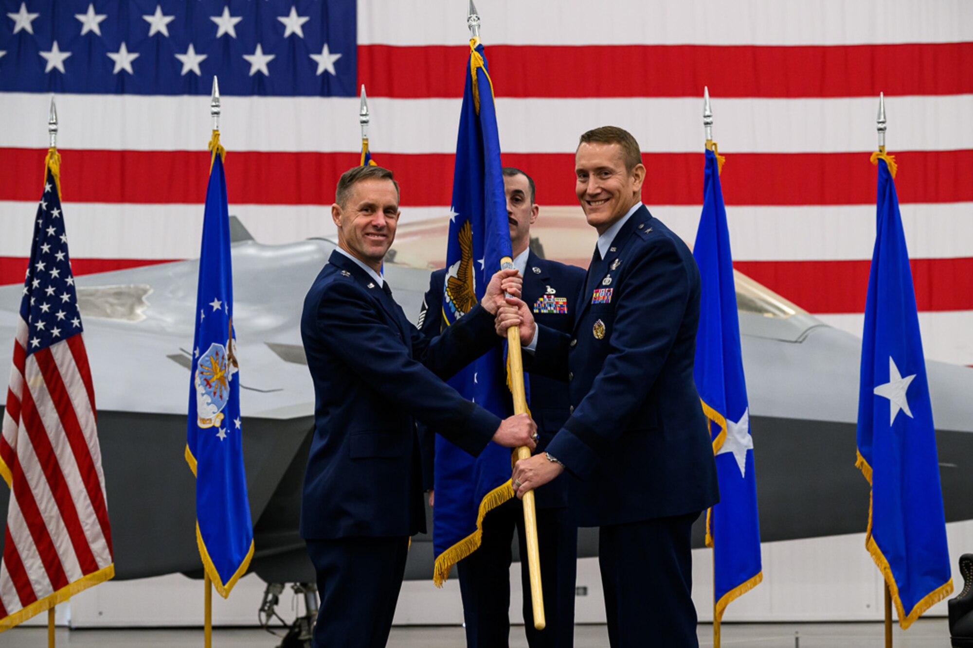 Man in uniform passes a flag to a second man in uniform