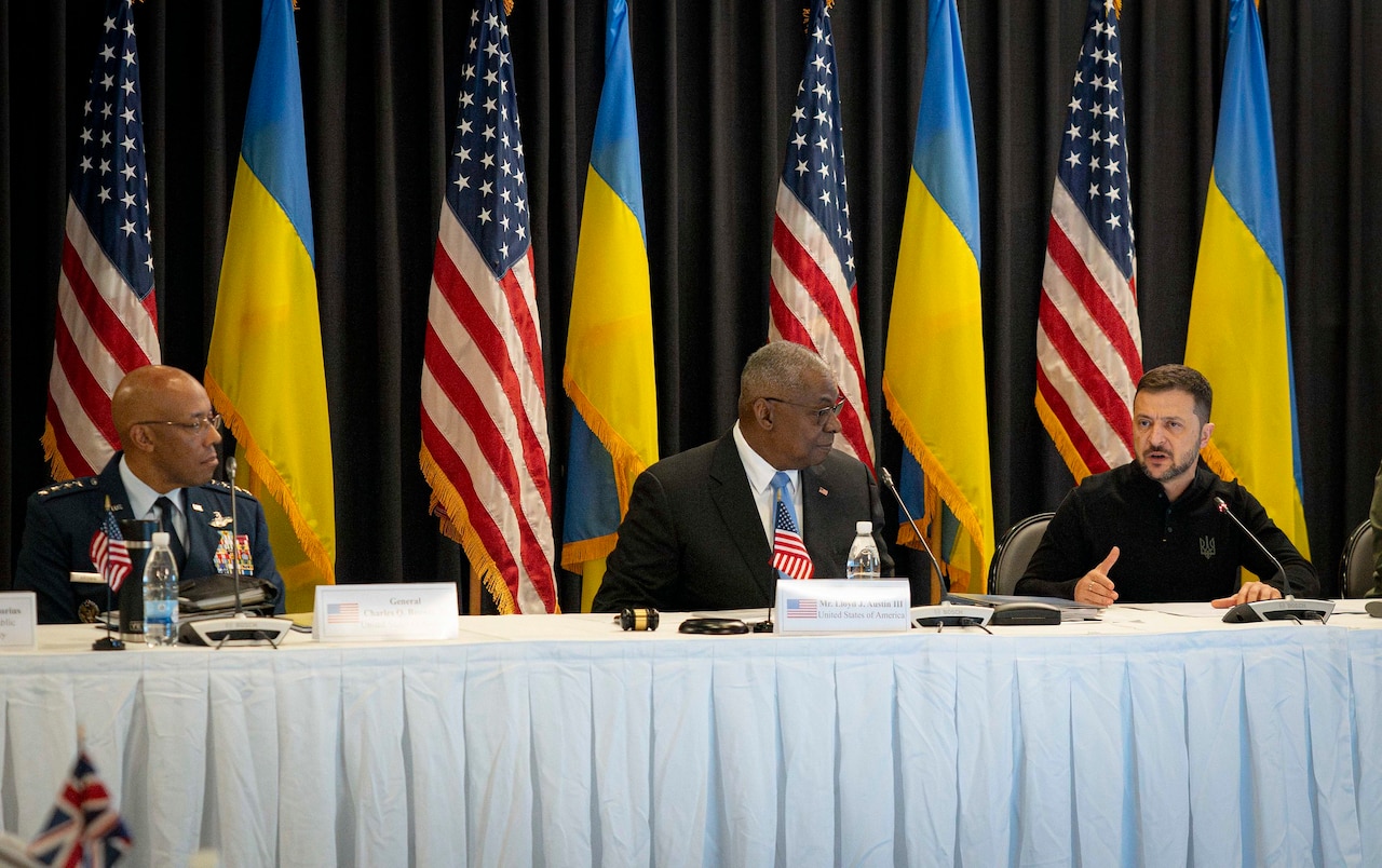 Three leaders sit on a white table with the U.S. and Ukrainian flags behind them.