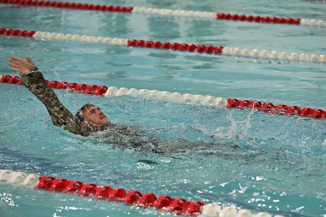 A soldier in uniform swims backstroke between red and white dividers in a pool.