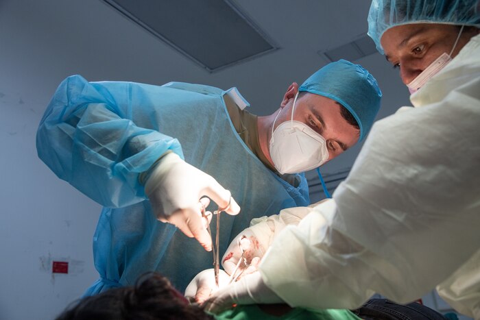 Two people with surgery tools operate on a woman.